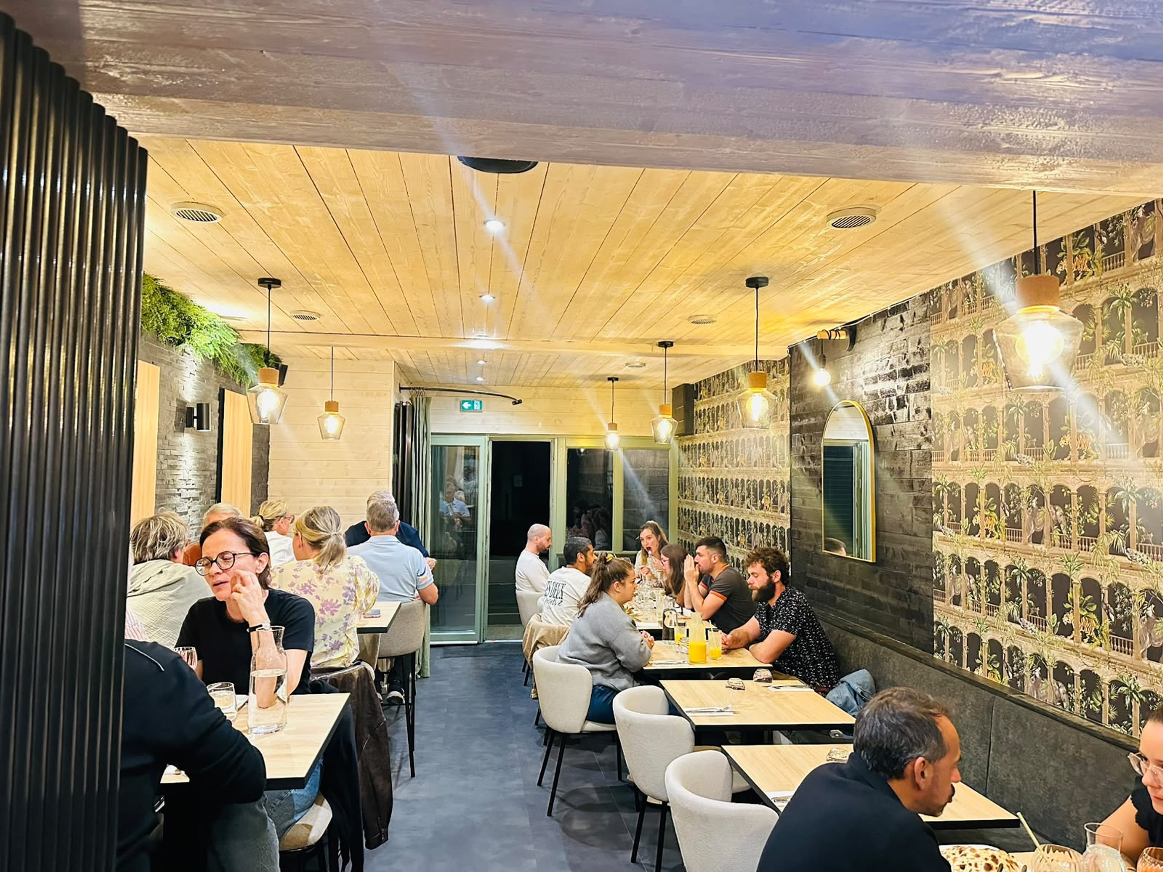Full dining room buzzing with guests beneath warm pendant lighting and patterned wallpaper