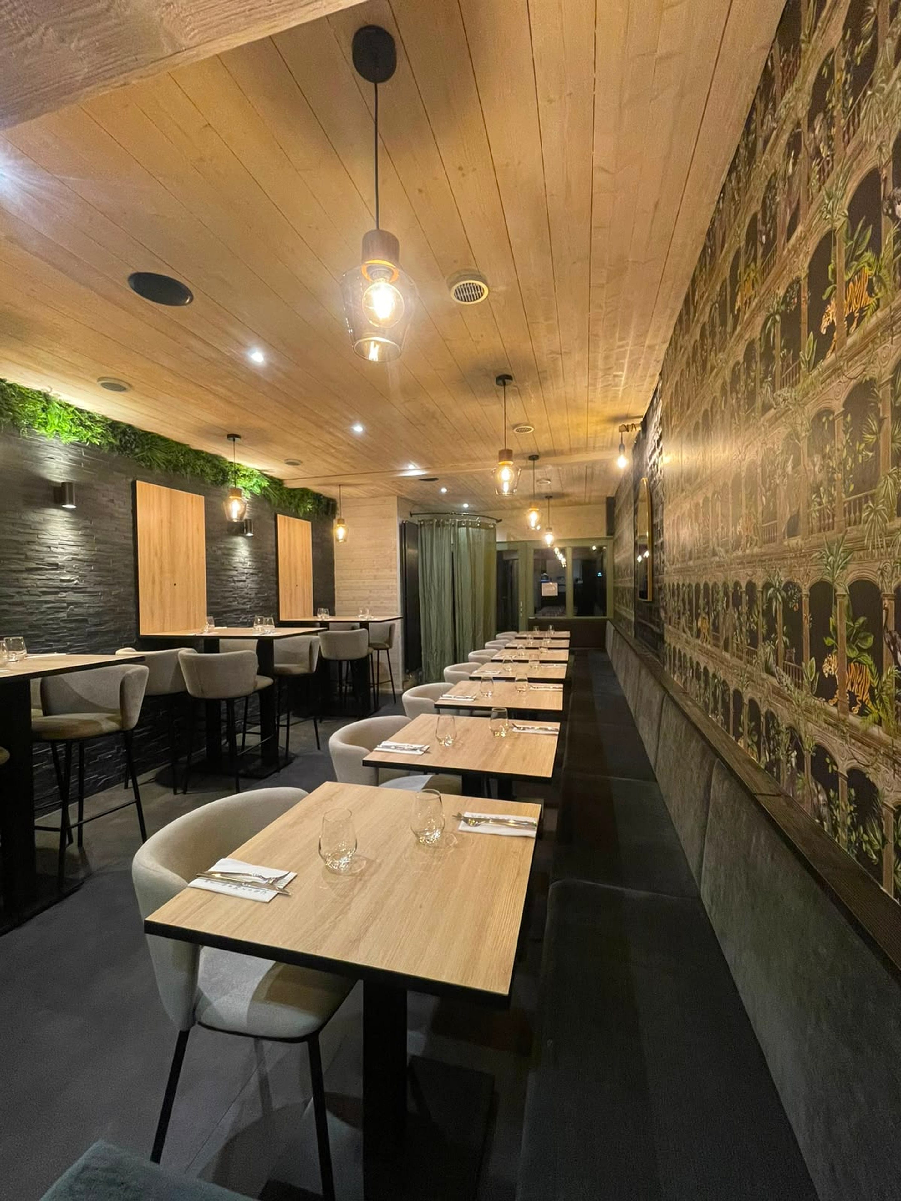 Long banquette dining room with jungle-print wallpaper and warm pendant lights
