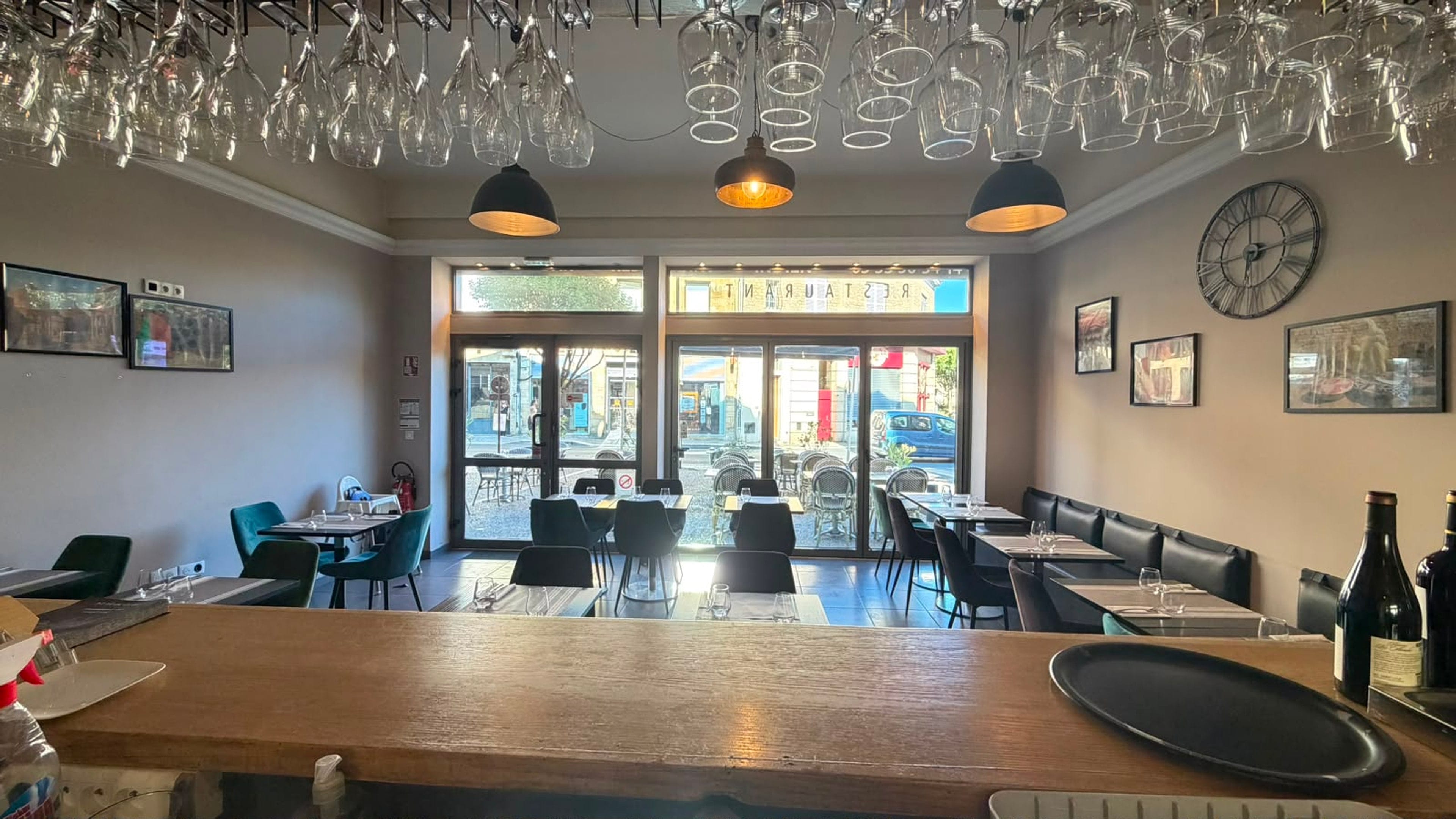 Bar counter view of the dining room with hanging wine glasses and street-facing windows