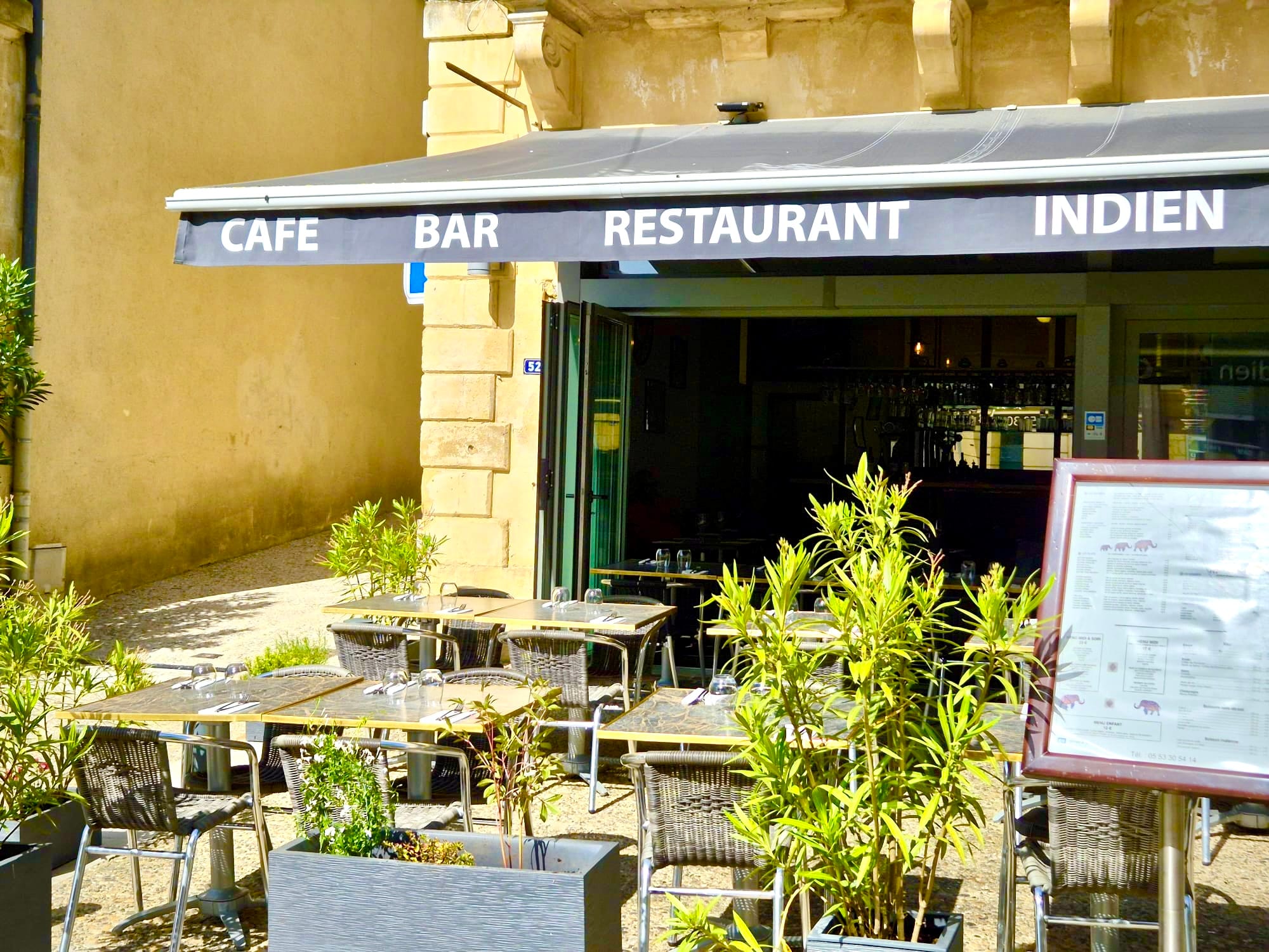 Sunlit cafe-bar-restaurant entrance framed by potted plants